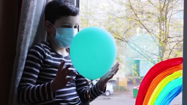 Ein Junge Mit Einem Blauen Ball Sitzt Fenster Quarantäne Regenbogen — Stockvideo