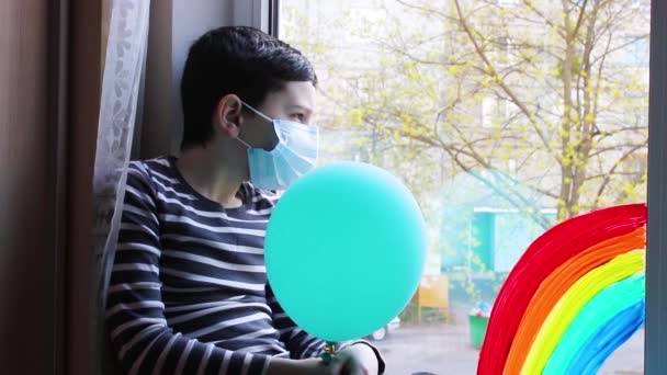Ein Trauriger Junge Mit Maske Sitzt Fenster Quarantäne Regenbogen — Stockvideo