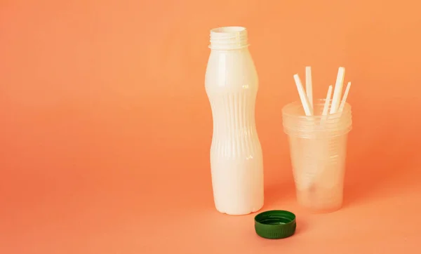 plastic dishes. Bottle and glass with spoons on a pink background. Plastic recycling concept. Banner. copyspace