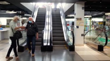 Süpermarket. Karantinaya alın. Maskeli insanlar yürüyen merdivende yürür. Erkek ve kadın eldiven takıyor