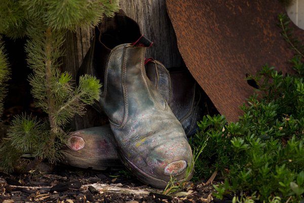 старые рабочие ботинки, упирающиеся в деревянный столб забора
