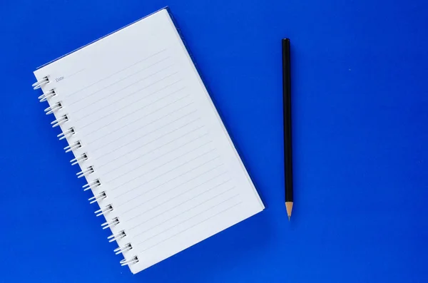 White note book and black pencil on blue color background with c Royalty Free Stock Images