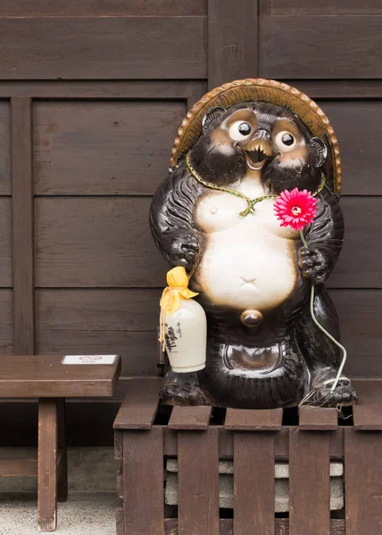 Statue Tanuki tient fleur rouge et la fiole de saké habituelle . — Photo