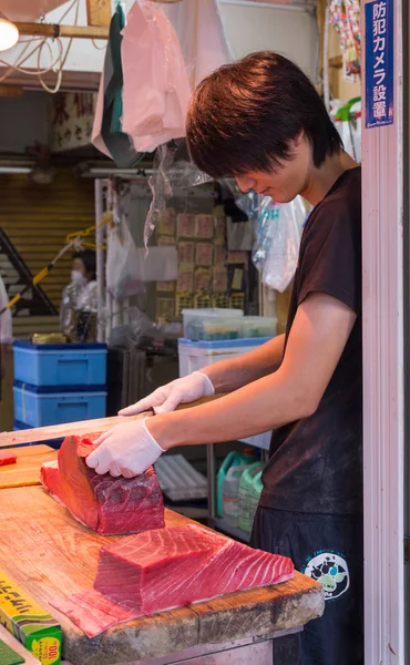 Un jeune homme coupe de la viande de thon au marché aux poissons de Tsukiji . — Photo