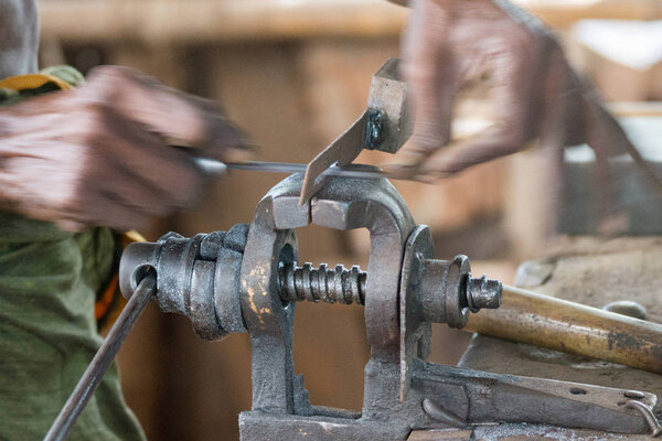 Dindigul, India - October 23, 2013: Closeup of hands moving fast back and forth while abrading, rubbing, filing a piece of metal lock held in a vise. The movement is visible.
