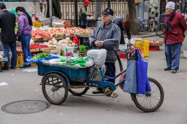 Yaşlı kadın kereviz piyasada mavi üç tekerlekli bisiklet kapalı satıyor.