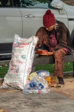 Evsiz kadın Da Nang Vietnam 'da bankta çantalarla oturuyor..