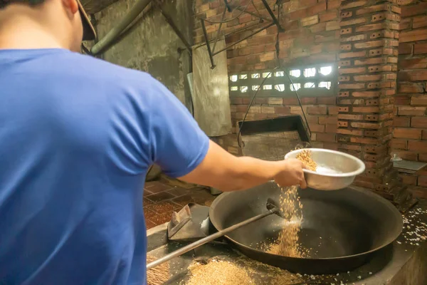 Man pours rice kernels to pop in black heated basin in Cai Be, M — ストック写真