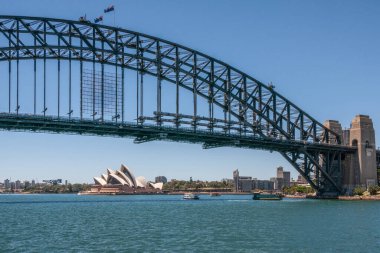 Sydney, Avustralya - 11 Aralık 2009: Harbour Köprüsü altında Opera Binası, metal kaplama, yay ve taş kuleler mavi gökyüzüne karşı ve gök mavisi körfez suyunun üzerinde. Birkaç tekne..