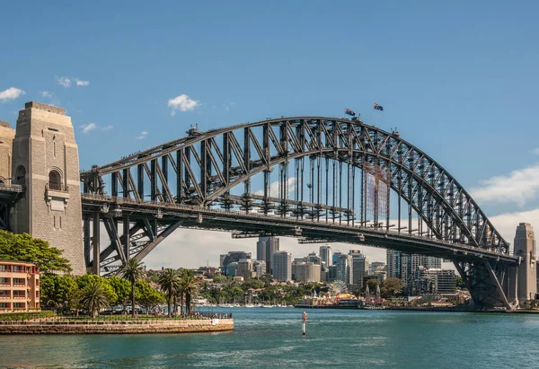 澳大利亚悉尼 2009年12月11日 海港大桥 全金属跨度 船首和石锚塔与蓝天和蓝色海湾水面相映成趣 北悉尼及露娜公园的高楼 — 图库照片