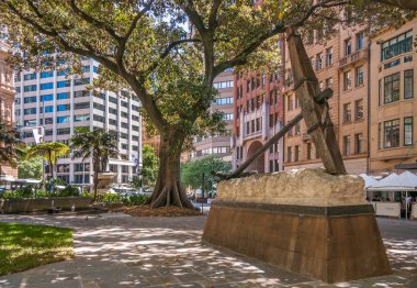 Sydney, Avustralya - 11 Aralık 2009: Macquarie Place Park 'ta tarihi çapa heykeli bulundu. Binaların ön cepheleri ve dev bir yeşil ağacın olduğu sokak sahnesi..