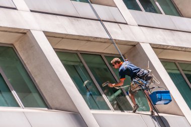 Sydney, Avustralya - 11 Aralık 2009: Erkek pencere temizleyicisi. Mavi ve kırmızı giyinmiş, bej rengi modern gökdelende çift ipten sarkıyor işini yapıyor..