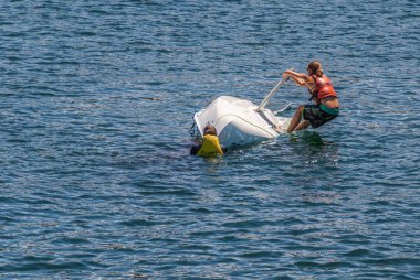 Sydney, Australia - December 11, 2009: Man and woman try manually to flip Capsized Magno Topaz small white sail boat back in dark blue bay water. 