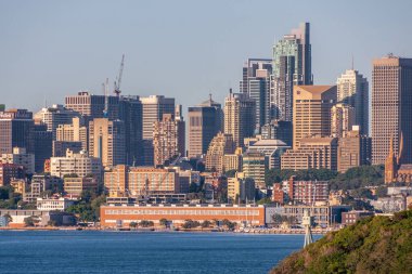 Sydney, Australia - December 11, 2009: City skyline with multiple skyscrapers and tallest World Tower. Navy pier and red warehouse-office on shore of bay. Green foliage of Bradleys Head.
