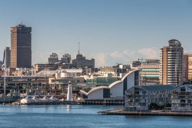 Sydney, Australia - December 11, 2009: White bows as roof of National Maritime Museum in Darling Harbour with dense cityscape in back under light blue sky and behind blue water.