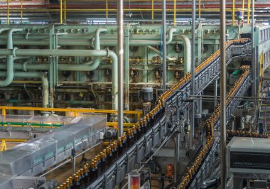 Brisbane, Australia - December 8, 2009: Castlemaine Perkins brewery. 2 lines of full bottles on their way to labeling machine on transport belts. Green bottle washer in back.