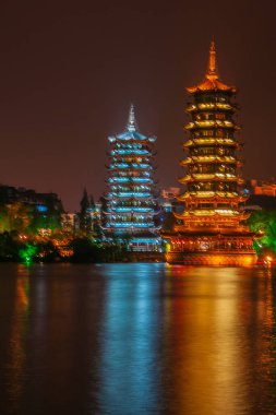 Guilin, China - May 9, 2010: Riyue Shuangta Cultural Park. The  Twin Pagodas in Shanhu Lake, the silver and the gold, under pitch black night. Their lights reflected in water. Other lights on shore.