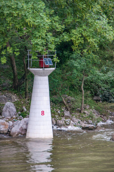 Guilin, China - May 10, 2010: Along Li River. White and red navigation beacon 8 standing in greenish water partly covered by green foliage.