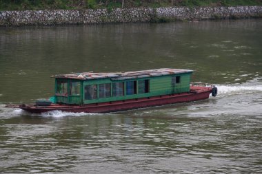 Guilin, China - May 10, 2010: Along Li River. Closeup of green-brown transport boat on dark greenish water. Pat of reinforced shoreline.