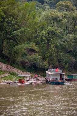 Guilin, China - May 10, 2010: Along Li River. Portrait of woman leaving raft at stairs hidden in green forest foliage on mountain slope with ferry docked  nearby.