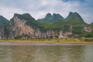Guilin, Çin - 10 Mayıs 2010: Li Nehri boyunca. Karst Dağları 'nın mavi bulutların altında kahverengi-siyah dikey uçurumlarla manzarası. Geniş ovalarda yeşil çalılar ve önde bataklıklar..