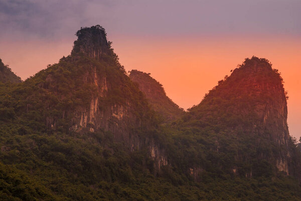 Guilin, China - May 10, 2010: Along Li River. Landscape of dark green covered karst mountains under red glowing sky.