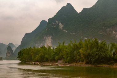 Guilin, Çin - 10 Mayıs 2010: Li Nehri boyunca. Küçük feribot manzarası, gri bulutların altında, Karst dağlarının önündeki yeşil ağaçların arasına kenetlenmiş..