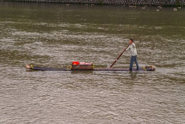 Guilin, Çin - 10 Mayıs 2010: Li Nehri üzerinde. Yakın plan, yeşil dalgalı su üzerinde soluk yeleği olan erkek satıcı. Kırmızı çantalı kahverengi sandık ve kovalarca mal..