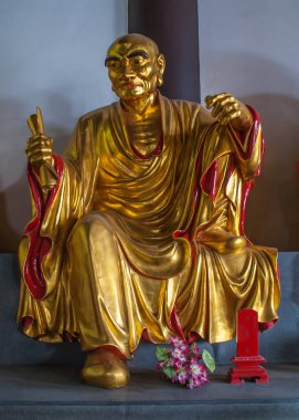 Guilin, China - May 11, 2010: Qixia Buddhist Temple in Seven Star Park. Golden statue of Arhat who meditates, Chinese Buddhist saint against blue backdrop.