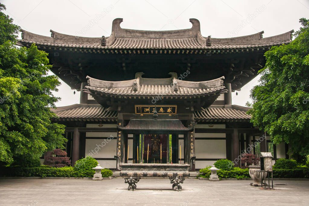 Guilin, China - May 11, 2010: Front facade of Qixia Buddhist Temple in Seven Star Park. Green foliage, silver sky and stone artistic incense vessel.