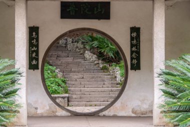 Guilin, China - May 11, 2010: Seven Star Park. Iconic circular doorway set in white wall with Mandarin symbols and showing on the other side a stone stairway. Green foliage adds color.