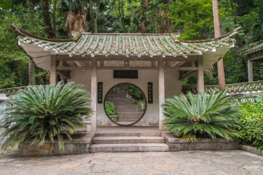 Guilin, China - May 11, 2010: Seven Star Park. Pavilion with circular doorway set in white wall with Mandarin symbols and showing on the other side a stone stairway. Green foliage adds color.