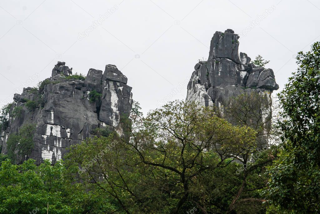 Guilin, China - May 11, 2010: Seven Star Park. Black and white camel mountain peeks over green foliage under silver sky.
