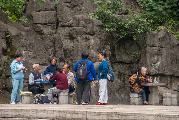 Guilin, China - May 11, 2010: Seven Star Park. Group of Chinese men and women play cards on two tables with black rock backdrop and some green foliage. Colors added by clothing.