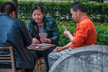 Guilin, Çin - 11 Mayıs 2010: şehir merkezi. Sandalye ve bankta, kadın ve iki erkek büyük bir dikkatle Çince kart oynuyorlar. Arkadaki yeşil yapraklar..