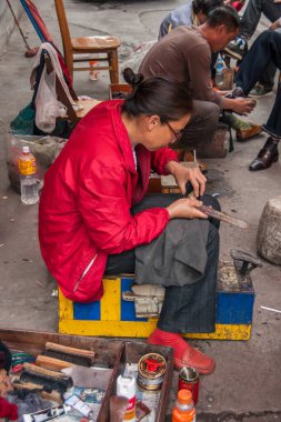 Guilin, Çin - 10 Mayıs 2010: şehir merkezi. İki meslektaşı arkada ayakkabı parlatırken, kırmızı ayakkabılı bir bayanın yaklaşması. Etrafta bir sürü tencere ve fırça olan sokak sahnesi.