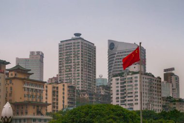 Chongqing, Çin - 9 Mayıs 2010: şehir merkezi. Kırmızı Çin bayrağı ve yeşil yapraklı farklı stil ve renklerde çeşitli ofis ve konut binaları. Açık mavi gökyüzü.