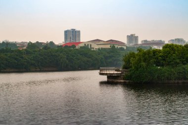 Chongqing, Çin - 9 Mayıs 2010: şehir merkezi. Kıyılarda yoğun yeşil ağaç yaprakları ve açık mavi gökyüzünün altında uzun binalar olan gümüş-kahverengi hapishane nehri..
