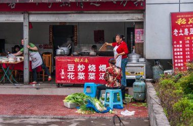 Chongqing, Çin - 9 Mayıs 2010: şehir merkezi. Üç kadın açık bir mutfak işletiyor, sebze kesiyor, garaj kapısının altındaki birkaç masada yemek pişiriyor ve müşterilere servis yapıyor.,