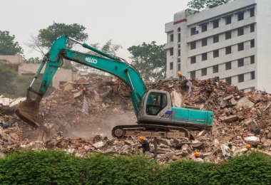 Chongqing, Çin - 9 Mayıs 2010, şehir merkezi, Peoples Meydanı. Yeşil Kobelco yıkım vinci taş moloz yığınının üstünde. Yeşil yapraklar ve arkadaki beyaz bina. İşçiler burada.