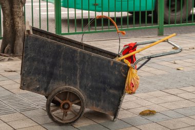 Chongqing, Çin - 9 Mayıs 2010: şehir merkezi. Sokakta çöp ve çöp toplamak için Kara Kutu 'nun itme arabası yaklaşıyor. Sarı süpürge sopası ve kırmızı güvenlik yeleği. Arkadaki yeşil çit..