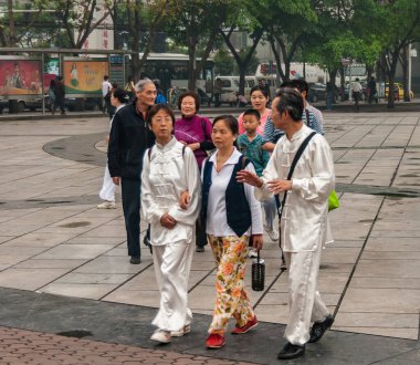 Chongqing, Çin - 9 Mayıs 2010: Halk otobüsü durağı ve cadde boyunca arabalarla şehir merkezinde gezinen aileler. Tai Chi antrenmanında 2 kişi ipek elbise giyer..