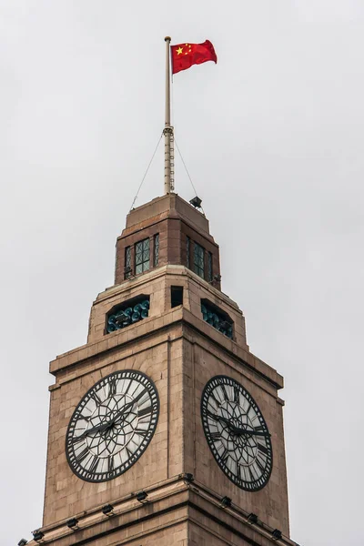 Shanghai, China - May 4, 2010: Closeup of light brown top of Custom House clock tower with red Chinese flag against silver sky. White and black clock included.