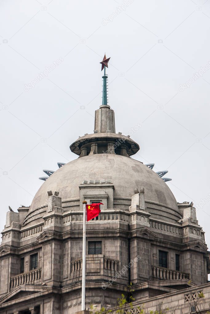 Shanghai, China - May 4, 2010: Closeup of gray-brown top with dome of HSBC bank with red Chinese flag in front, star on top, against silver sky.