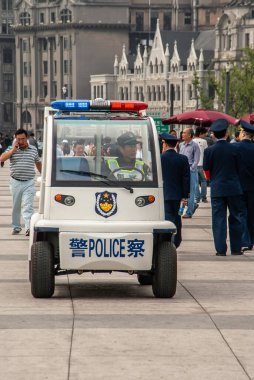 Şangay, Çin - 4 Mayıs 2010: Huangpu Nehri boyunca yayalarla dolu tahta kaldırımda görevli memurla birlikte beyaz-mavi polis elektrikli aracına yakın çekim. Arkaplan olarak binalar.