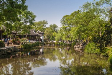 Suzhou Çin - 3 Mayıs 2010 Mütevazı Yöneticiler Bahçesi. Yansıyan su ve ikonik bina ile daha geniş bir kanal. Açık mavi gökyüzünün altında iki tarafta da yeşil ağaçlar var. İnsanlar serpiştirildi.