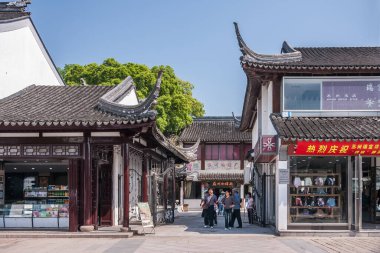Suzhou China - 3 Mayıs 2010: Küçük dükkanlar olarak düşük beyaz ve gri binaları olan alışveriş caddesi. Yayalar yürüyor. Yeşil yapraklar ve mavi gökyüzü.
