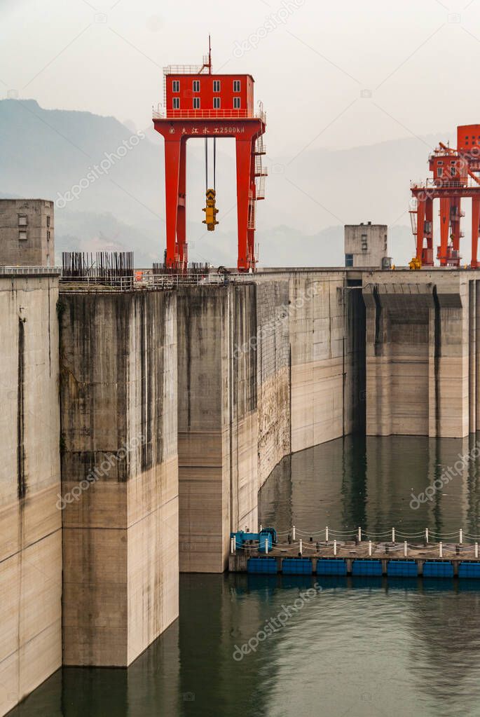 Three Gorges Dam, China - May 6, 2010: Yangtze River. foggy Morning, up-river portrait closeup along the brown concrete wall with red crane on top on greenish water. Blue ponton pier.