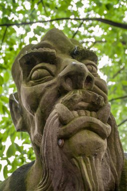 Fengdu, Çin - 8 Mayıs 2010 Hayalet Şehir, tarihi sığınak. Öfkeli, agresif erkek yüzünün önden yakın çekimi. Büyük dişleri ve sakalı var. Gri heykelin üzerinde ve Çaresizlik Köprüsü 'nde yeşil deri kaplı..