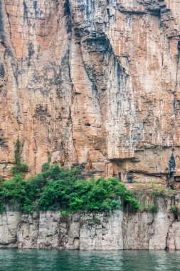 Wuchan, Çin - 7 Mayıs 2010: Daning Nehri 'ndeki Ejderha Kapısı Boğazı. Uzun kahverengi ve siyah uçurum zümrüt yeşili suya iniyor. Altta yeşil yapraklar. 